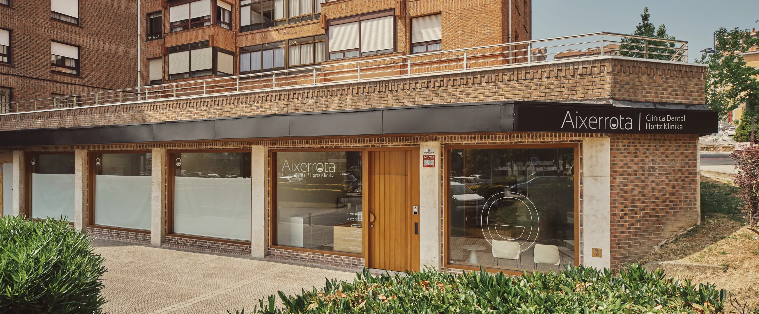 Fachada de la Clínica Aixerrota en la esquina de un edificio de ladrillo, con ventanales y puerta de madera