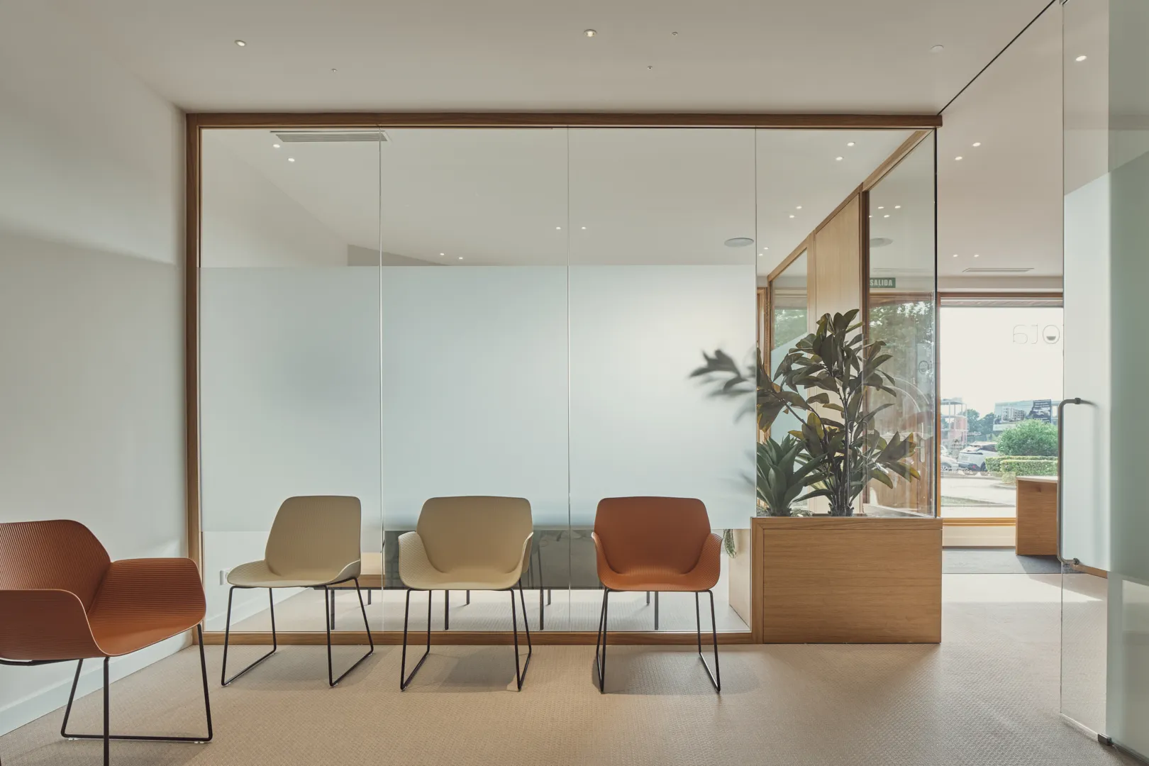 Sala de espera con sillas de colores y una planta tras una cristalera