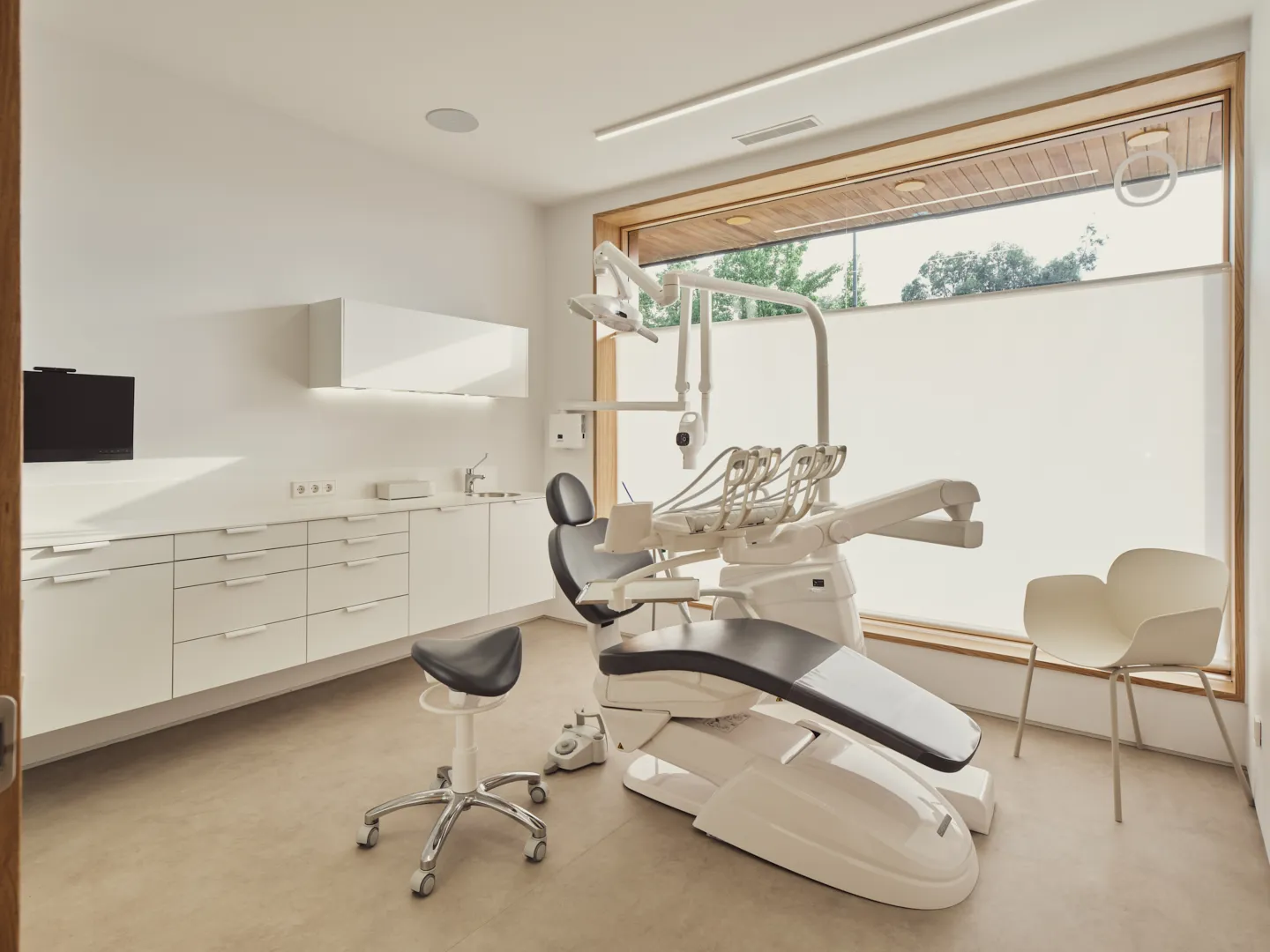 Gabinete dental con sillón, mobiliario blanco y un gran ventanal